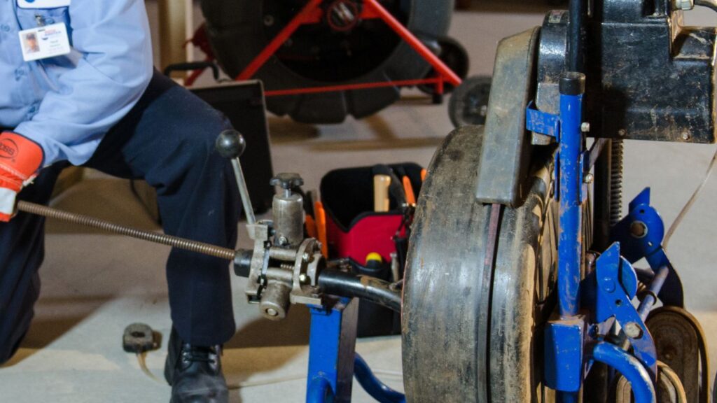 man using a rooter tool to unclog a bathroom pipe